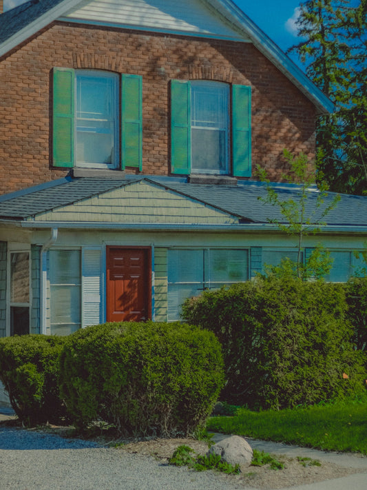 A cozy brick house stands with green shutters.